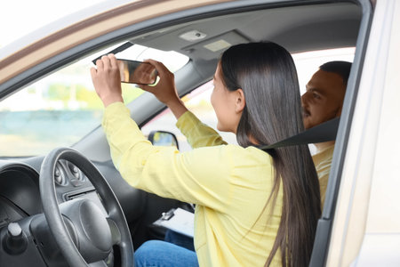 Young woman adjusting mirror before passing driving license test with instructor in car