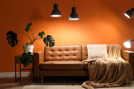 Interior of living room with brown sofa, plant and glowing lamps