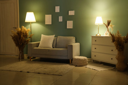 Interior of living room with gray sofa, frames and glowing lamps