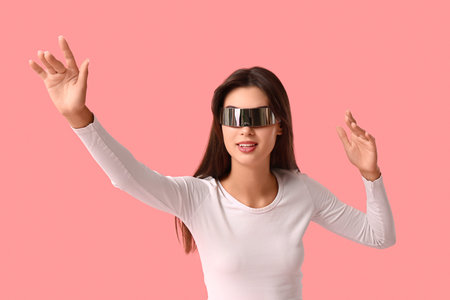 Beautiful young woman in modern VR glasses on pink background