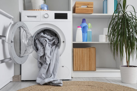 Interior of light laundry room with washing machine, bed sheets and shelf unit