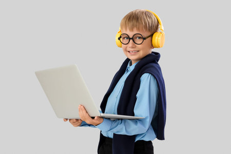 Little schoolboy in headphones with laptop studying computer sciences on light background