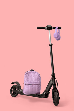 Modern electric scooter with headphones and backpack on pink background