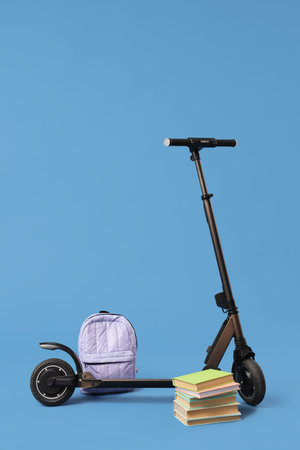 Modern electric scooter with backpack and books on blue background