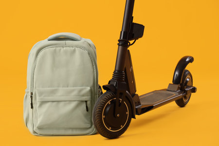 Modern electric scooter with backpack on yellow background, closeup