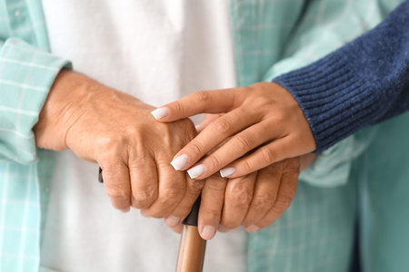 Female caregiver and senior woman with walking stick at home, closeup