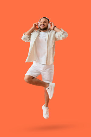 Handsome young man in headphones jumping on orange background