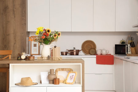 Interior of light kitchen with table, counters and autumn flowers in vase