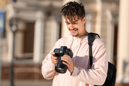 Young happy male photographer with camera and backpack on street
