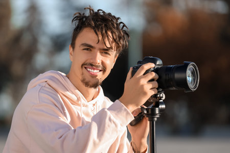 Young happy male photographer with camera and tripod on street