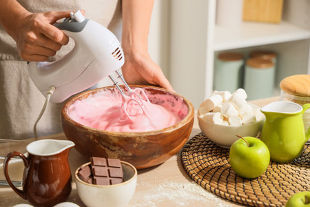 Woman whipping pink egg albumen with mixer in kitchen, closeup