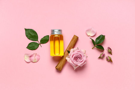 Composition with bottle of rose and cinnamon essential oil on pink background