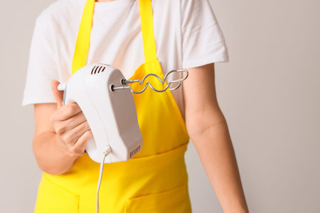 Woman with mixer on light background, closeup