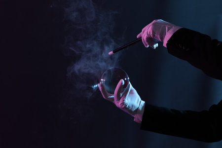 Male magician's hands with crystal ball and wand on dark backgroundの写真素材