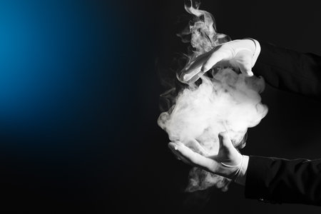Male magician's hands with smoke on dark backgroundの写真素材