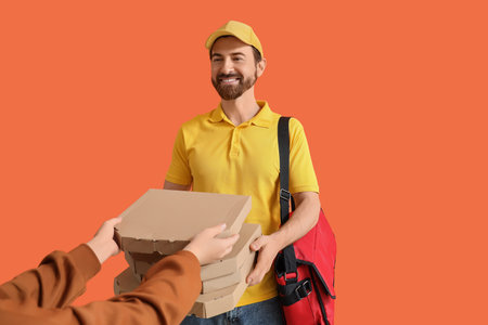 Male courier delivering pizza boxes to customer on orange backgroundの写真素材