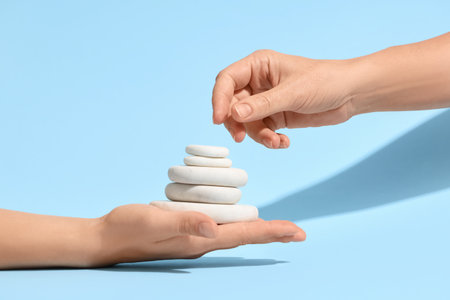 Hands with stack of pebbles on blue background. Zen conceptの写真素材