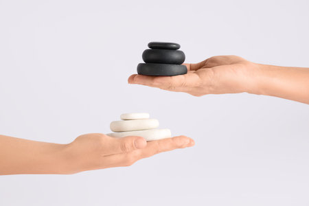 Hands with stacks of pebbles on light background. Zen concept