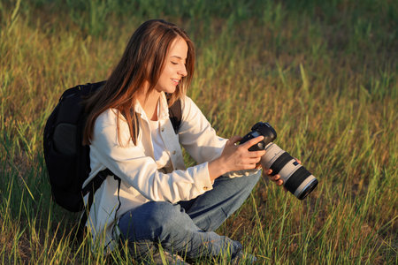 Young female photographer with camera sitting in park at sunsetの写真素材