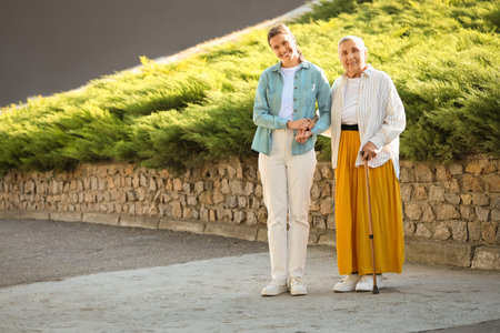 Senior woman with stick and caregiver on streetの写真素材