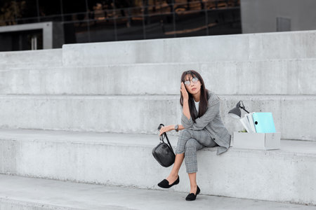 Asian businesswoman with personal stuff sitting on step outdoorsの写真素材