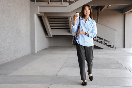Young Asian businesswoman with wristwatch and coffee walking outdoors. Time management conceptの写真素材