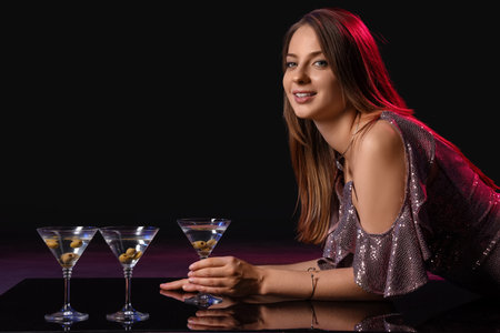 Beautiful woman with martini at table on dark backgroundの写真素材