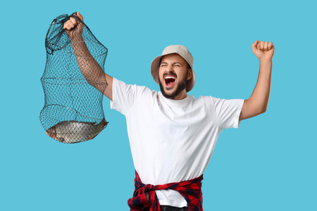 Happy young man with caught fish in keepnet on blue backgroundの写真素材