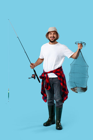 Handsome young man with fishing rod and keepnet on blue background