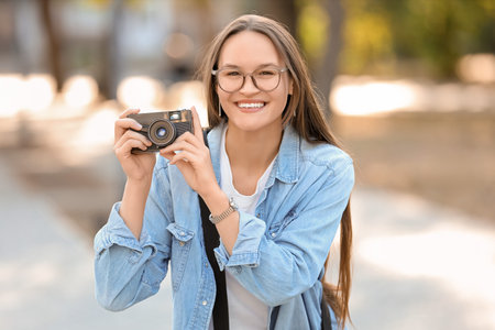 Young happy female photographer with digital camera and bag in park