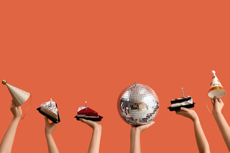 Female hands with disco ball, Birthday cakes and party hats on orange backgroundの写真素材