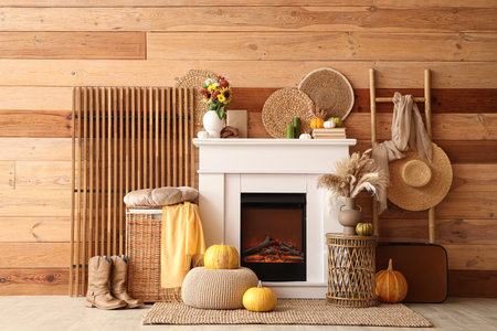 Interior of living room with folding screen, ladder, suitcase, wicker table and autumn decorations on fireplace near wooden wallの写真素材