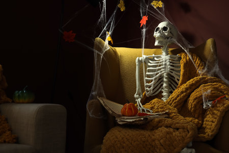 Human skeleton with book on armchair in dark living room decorated for Halloweenの写真素材