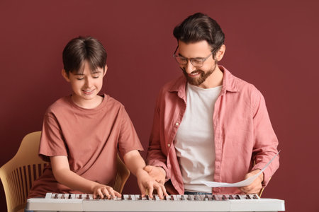 Private music teacher giving synthesizer lessons to boy on burgundy backgroundの写真素材