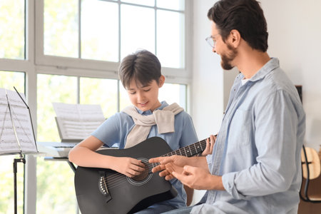 Cute boy taking guitar lessons from private music teacher in roomの写真素材
