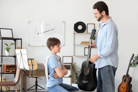 Private music teacher showing guitar to boy in roomの写真素材