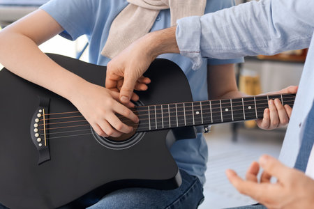 Boy taking guitar lessons from private music teacher in room, closeup