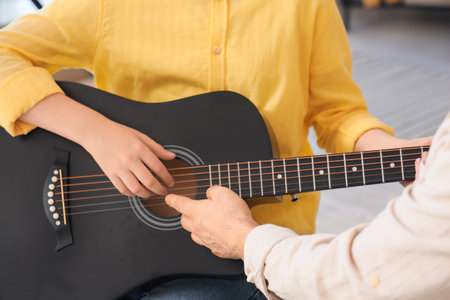 Private music teacher giving guitar lessons to boy in room, closeup