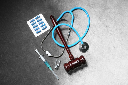 Judge gavel with stethoscope, pills, ampule and syringe on grunge gray background. Concept of health care reformの写真素材