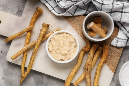 Composition with cutting board, bowls with horseradish sauce and roots on gray grunge background, closeupの写真素材