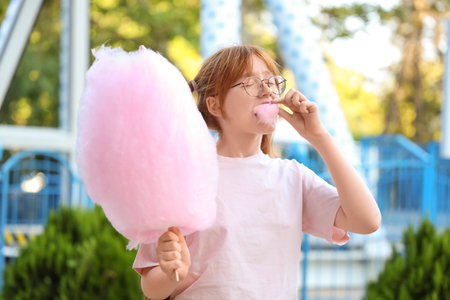 Teen girl eating cotton candy in amusement parkの写真素材