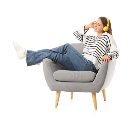 Young woman with headphones in gray armchair on white backgroundの写真素材
