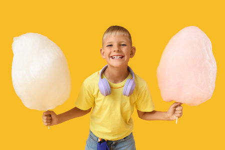 Teen boy with two sticks of cotton candy and headphones on yellow backgroundの写真素材