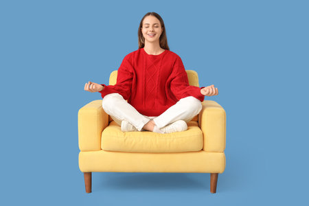 Young woman meditating in yellow armchair on blue backgroundの写真素材