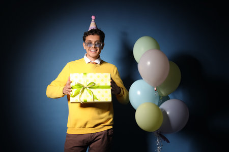 Happy young man with Birthday gift and balloons on dark blue backgroundの写真素材