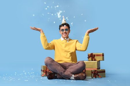 Happy young man with gifts celebrating Birthday on blue backgroundの写真素材