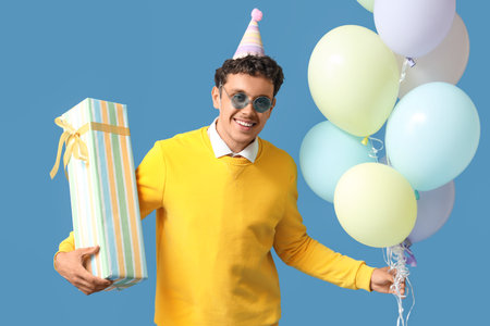 Happy young man with Birthday gift and balloons on blue backgroundの写真素材