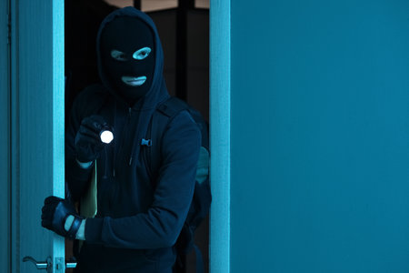 Male thief with flashlight breaking through door of house at nightの写真素材
