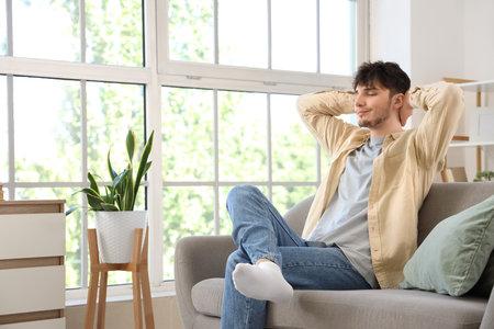 Dreaming young man sitting on sofa at homeの写真素材