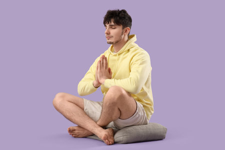 Young man meditating on lilac backgroundの写真素材